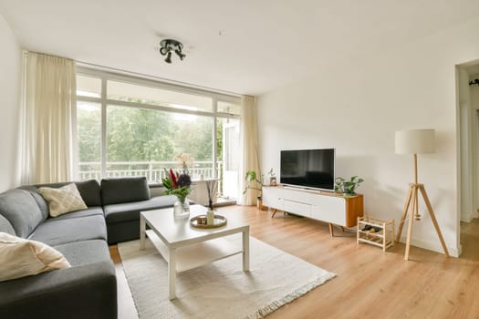 A stylish, modern living room featuring a comfortable gray sofa, wooden furniture, and large windows allowing natural light to fill the space.