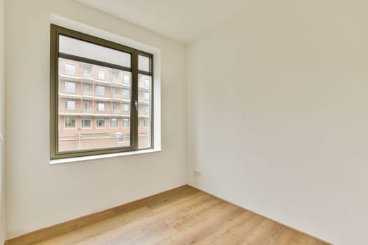A spacious, minimally decorated room featuring a large window that lets in natural light, creating a bright atmosphere with wooden flooring.