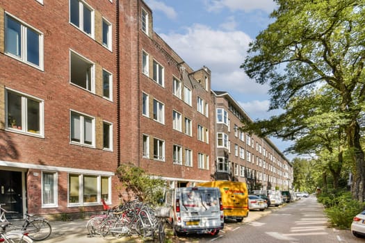 A serene residential street lined with brick buildings, featuring parked bikes and vehicles amidst lush greenery.