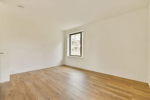 A spacious, modern interior featuring clean lines and light wooden flooring. The room is bright with natural light streaming in through a large window.