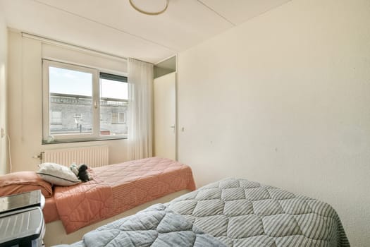 A serene bedroom featuring two neatly made beds, a large window allowing natural light, and simple, minimalistic decor that creates a calming atmosphere.