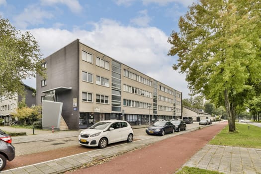A contemporary architectural design showcases a modern building alongside well-maintained greenery and parked cars on a city street.