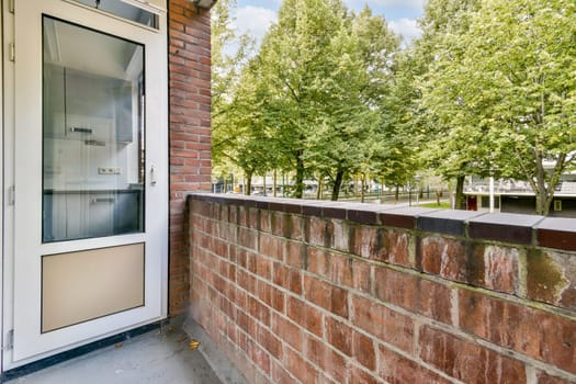 A bright view of an urban balcony with a glass door, brick wall, and lush trees in the background providing a peaceful escape in the city.