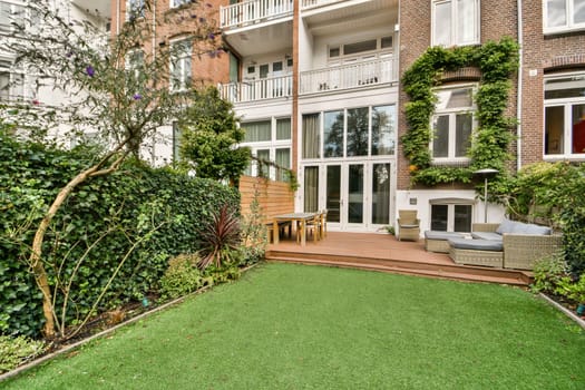 A contemporary outdoor space featuring lush greenery, a wooden patio area, and stylish plants, ideal for relaxation and outdoor gatherings in an urban setting.