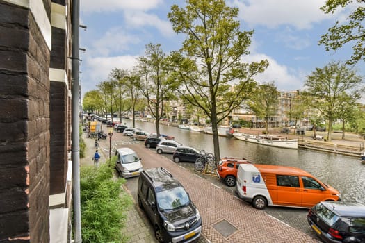 View of a picturesque canal street lined with trees and parked vehicles, showcasing urban life and nature coexisting.