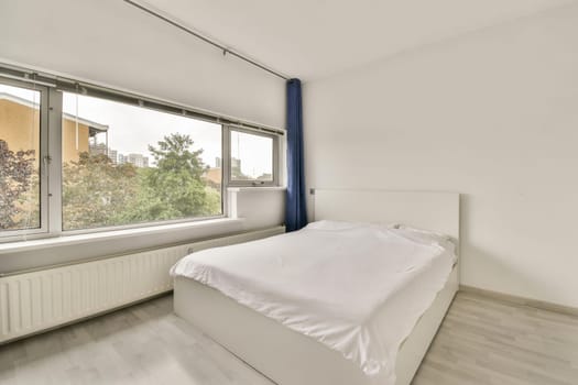 A spacious minimalist bedroom featuring a window with a view and a neatly made bed. The design emphasizes simplicity and natural light.