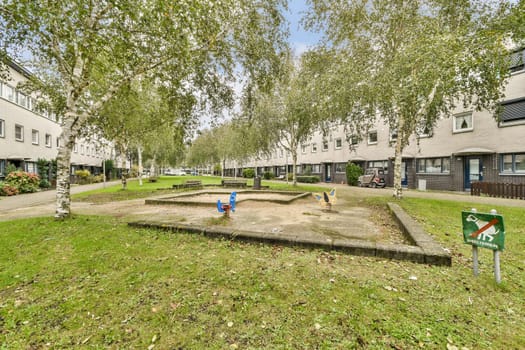 A peaceful residential neighborhood featuring green trees, a small play area, and modern buildings. Ideal for family living in an urban setting.