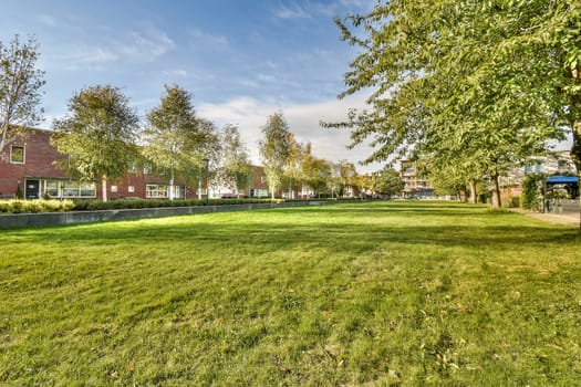 A serene park setting featuring lush trees and a well-maintained lawn, surrounded by buildings. Ideal for recreational activities and relaxation in an urban environment.