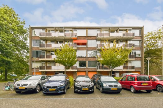 A multi-story apartment building featuring a parking area with various cars. Well-maintained greenery enhances the outdoor space.