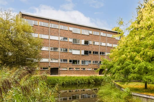 A multi-story residential building displayed against a backdrop of lush greenery and a serene body of water, reflecting the structure beautifully.