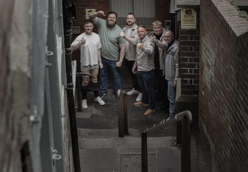 Newcastle, UK - Apr 12, 2025 - Group of cheerful male friends gathered with thumbs up emotionally and smiling posing for a portrait on the stairs leading down a narrow alley. Positive and Friendly expression, use it as your Wallpaper, Poster and Space for text, Selective focus.