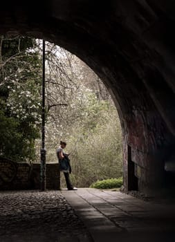 Newcastle, UK - Apr 12, 2025 - Lonely woman in t-shirt and jeans leans against brick railing and looking at a message on her smartphone under the high level bridge at afternoon sunlight. use it as your Wallpaper, Poster and Space for text, Selective focus.