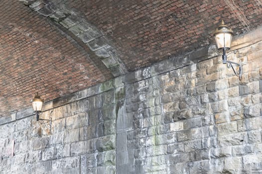 Newcastle, UK - Apr 12, 2025 - Two lantern lighting a spot on stone wall and red brick ceiling in tunnel under the high level bridge. An curved brick tunnel with lamps under the bridge, use it as your Wallpaper, Poster and Space for text, Selective focus.