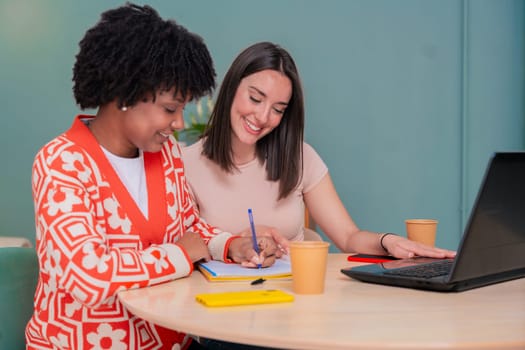 Caucasian and African American students work together using a laptop and notebook. Focused and cheerful, they collaborate in a cozy indoor space, representing learning, diversity, and teamwork.