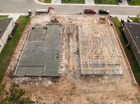 Aerial view of newly poured concrete slab next to home that is being constructed with wooden framework in Georgetown Texas