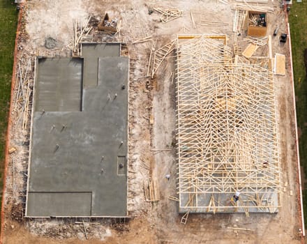 Aerial view of newly poured concrete slab next to home that is being constructed with wooden framework in Georgetown Texas