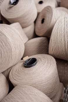 Close-up of multiple beige yarn cones stacked for textile manufacturing in a fabric or knitting production facility.