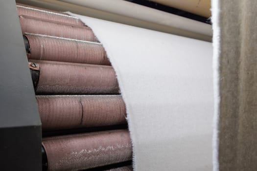 Industrial textile production process with white fabric passing through spinning rollers in a modern factory.