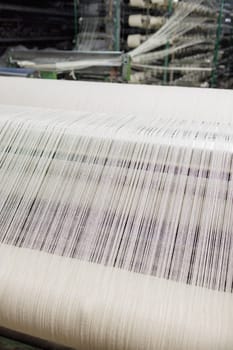 Automated textile production with white threads on a weaving loom machine in a modern fabric manufacturing plant.