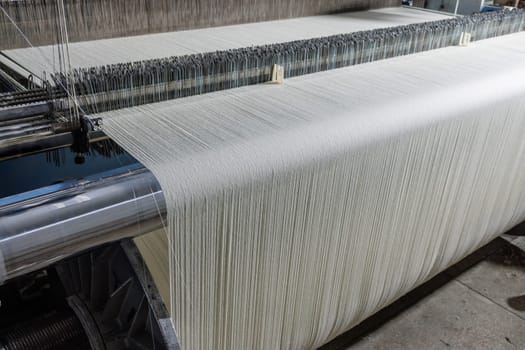 Automated textile loom weaving white yarn into fabric in a modern factory, showcasing precision threadwork.