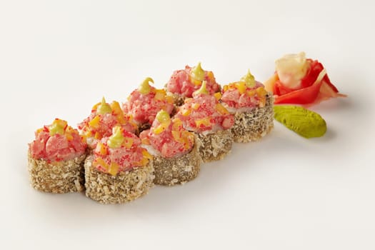 Delicious tempura sushi rolls topped with spicy tuna, mango, and tobiko, served with wasabi and ginger on a white background