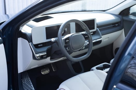 Steering wheel of a electric vehicle, interior cockpit, electric buttons, digital speedometer, front seats, textile, windows, console, gear shift. Car dashboard with a digital touchscreen.