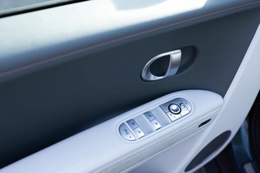 Car window controls. Door handle with power window control. Window control buttons in modern luxury electric car. Car leather interior details of door handle with windows controls and adjustments.