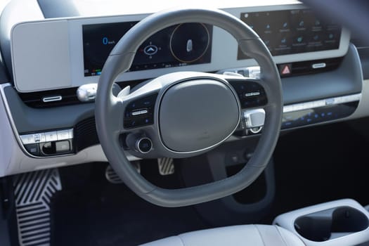 White leather dashboard, climate control, speedometer, display, wood decoration. Car steering wheel. Expensive electric car interior with steering wheel.