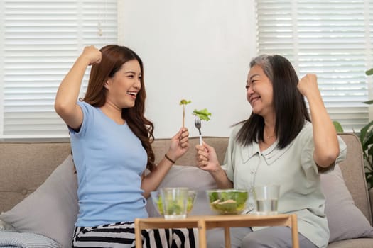 A cheerful moment shared between a mother and daughter as they celebrate their healthy choices with a playful salad cheer, representing joy and wellness.