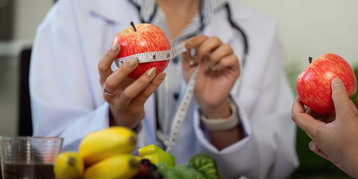 A nutritionist assesses the size of an apple using a measuring tape, educating the patient about portion sizes and healthy eating habits.