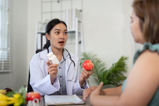 In a professional setting, a nutritionist discusses the importance of medication and healthy eating, illustrating concepts with apples and a supplement bottle.