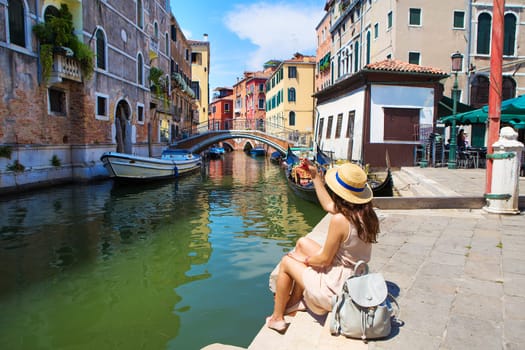 beautiful girl in a hat sits near a canal in Venice, Italy.