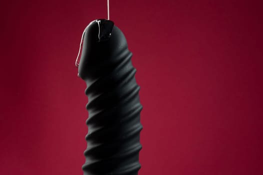 Lube pouring on black dildo on pink background