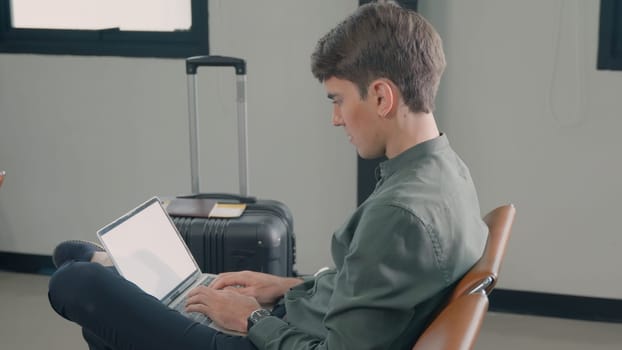 Young handsome man with a suitcase sitting working his laptop at airport terminal hall while waiting landing for her flight, tourist men in international airport, travel trip