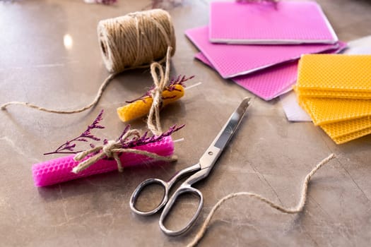 Colorful rolled beeswax candles with twine and scissors on a marble surface.