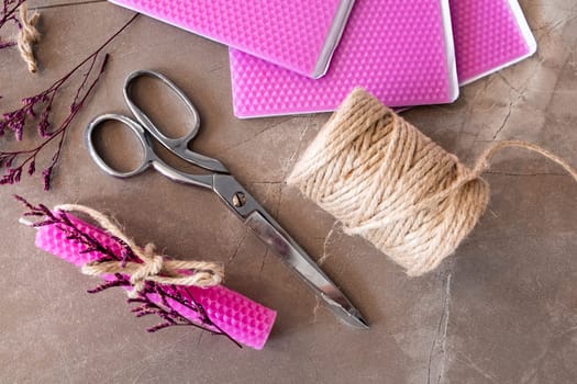 Crafting materials with pink wax sheets, scissors, jute twine, and dried flowers on stone surface.