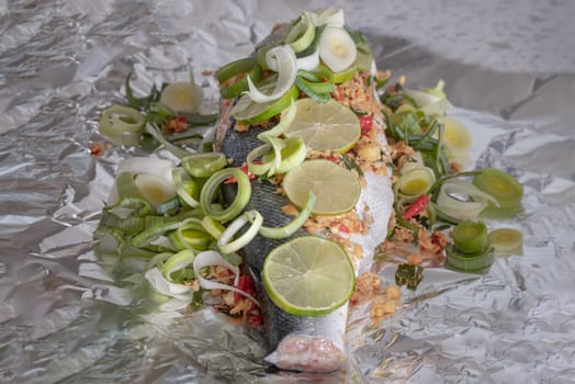 Prepare Whole Baked Salmon with Herbs on aluminium foil. ingredient include Coriander root, Ginger, Galangal, Kaffir lime, Leek, chopped together and Bird's eye chili with Slice lemons place on the Salmon fish. Healthy eating, use it as your Wallpaper, Poster and Space for text, Selective focus.