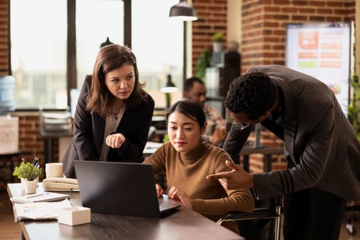 Male and female employees discussing marketing plans in modern workspace, using technology to research industry trends. They are sharing ideas and analyzing financial data on laptop in startup company.