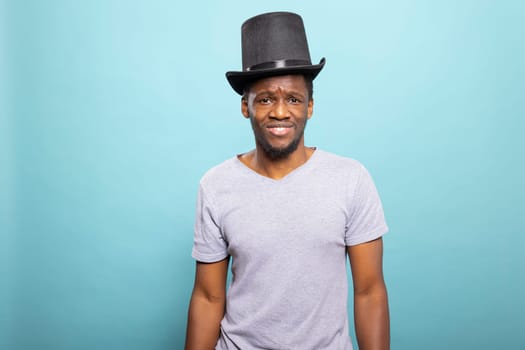 Portrait of a confused adult wearing a vintage black top hat, looking at the camera. African American individual with a magician hat and puzzled expression, standing against an isolated background.