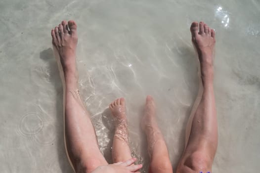 Top view of the legs of a one year old boy and his mother on the seashore