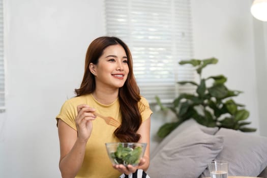 With joy, a woman smiles while eating a nutritious salad, showcasing the importance of healthy habits and a positive attitude towards life and well-being.