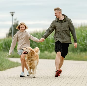 Dad With Daughter And Golden Retriever Dog Run Along The Path