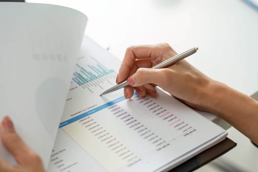 Dedicated to analyzing her report, a woman closely inspects financial data, noting important trends and insights as she prepares for an upcoming presentation.
