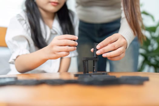 The image captures a thoughtful moment where the mother guides her daughter in stacking dominos, showcasing parental support and creativity in a family environment.