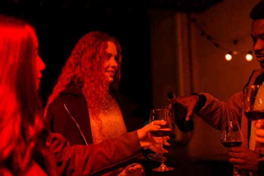 Group of friends share laughter and drinks in a warmly lit setting. The ambiance is inviting, with red lighting enhancing the cozy vibe of the evening gathering.