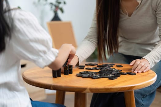 A mother assists her daughter in stacking dominoes, creating a playful yet educational environment that encourages creativity and learning.