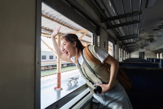 Waving enthusiastically from the window of a train, a young woman captures the spirit of adventure and exploration during her journey.