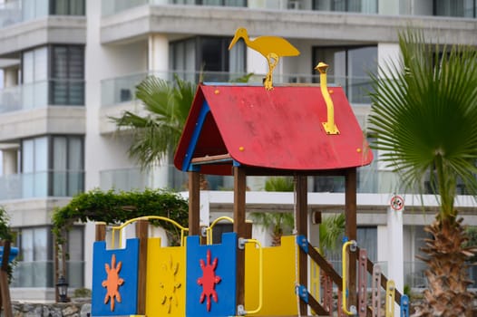 A vibrant playground structure featuring playful designs sits beneath tall palm trees beside a sleek apartment building. The cheerful colors invite children to explore and create fun memories.