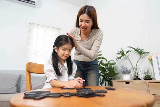 A mother gently encourages her daughter as they play a game of strategy with dominos, highlighting love, laughter, and developmental learning in a cozy home setting.