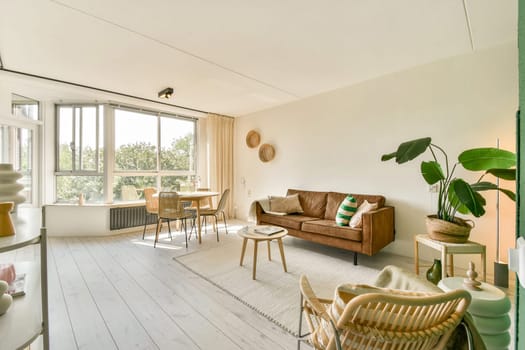A stylish living room featuring a blend of natural light, modern furniture, and greenery. The space is inviting, showcasing design aesthetics with comfort.